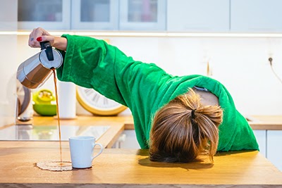 Sleepy woman pouring coffe on a table out of the mug