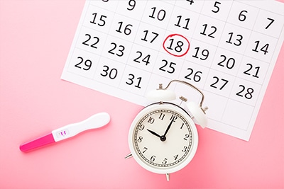 Pregnancy test next to a calendar and a watch