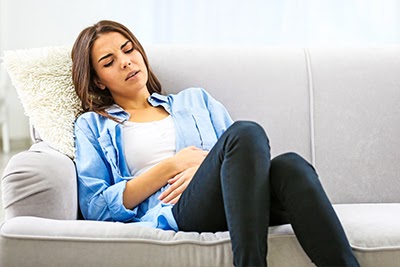 Young woman sitting on couch, suffering from ovulation crapms