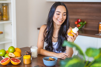 Smiling woman with a bottle of vitamins sitting at the kitchen table