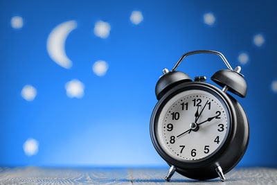 Round alarm clock in a blue background with moon and stars