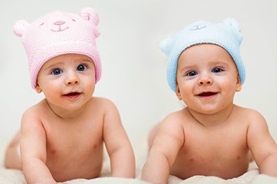 baby girl with pink cap and baby boy with blue cap, looking curiously at the camera