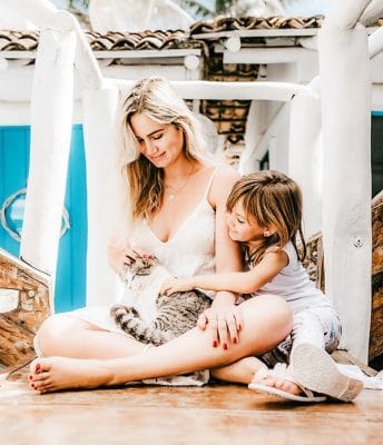 Mother sitting at home with her child on the porch petting a cat.