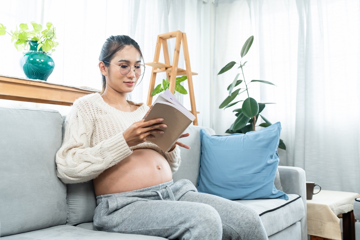 Pregnant woman sitting on a couch, reading a book
